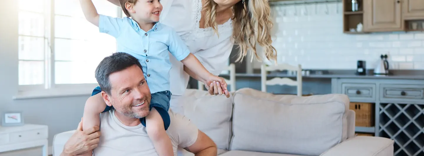Una famiglia sorridente composta da padre, madre e figlio piccolo che giocano insieme nel soggiorno di casa.