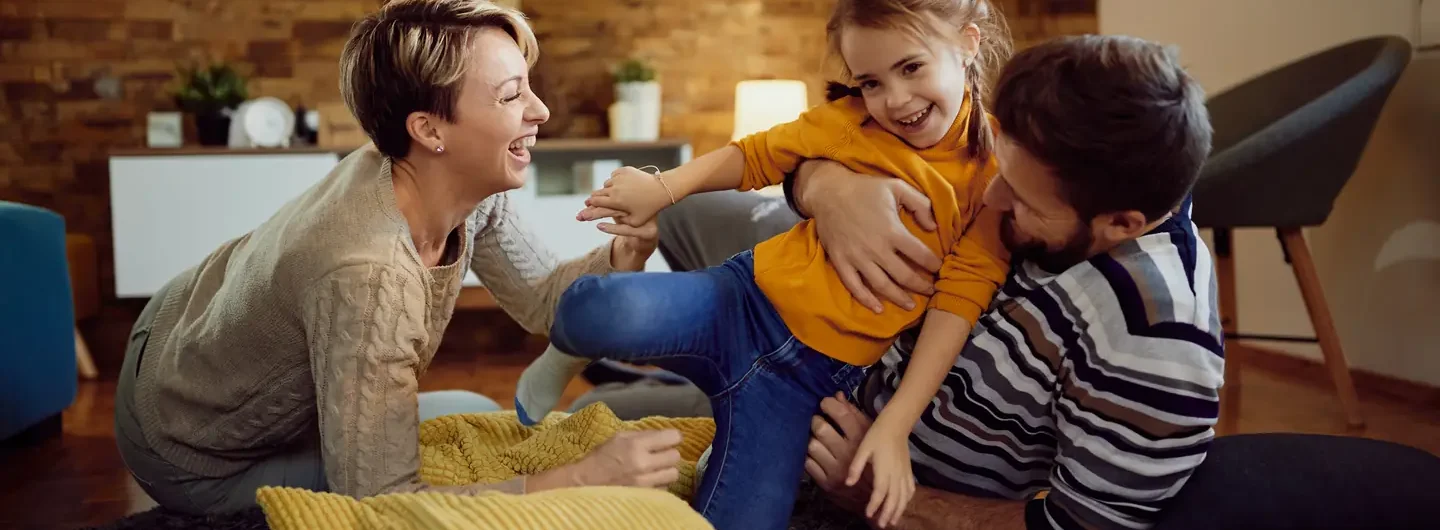 Una famiglia gioca insieme sul pavimento del soggiorno in un ambiente domestico sereno e protetto.