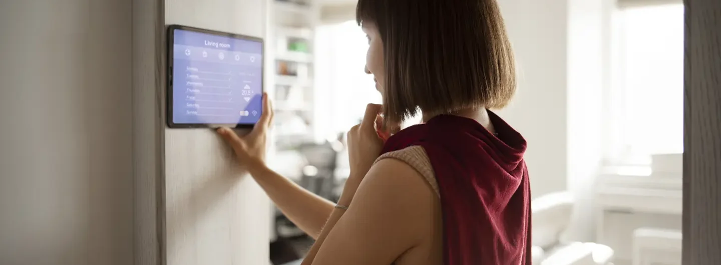 Una donna utilizza un pannello touch screen a parete per gestire il sistema di sicurezza e domotica della propria casa.